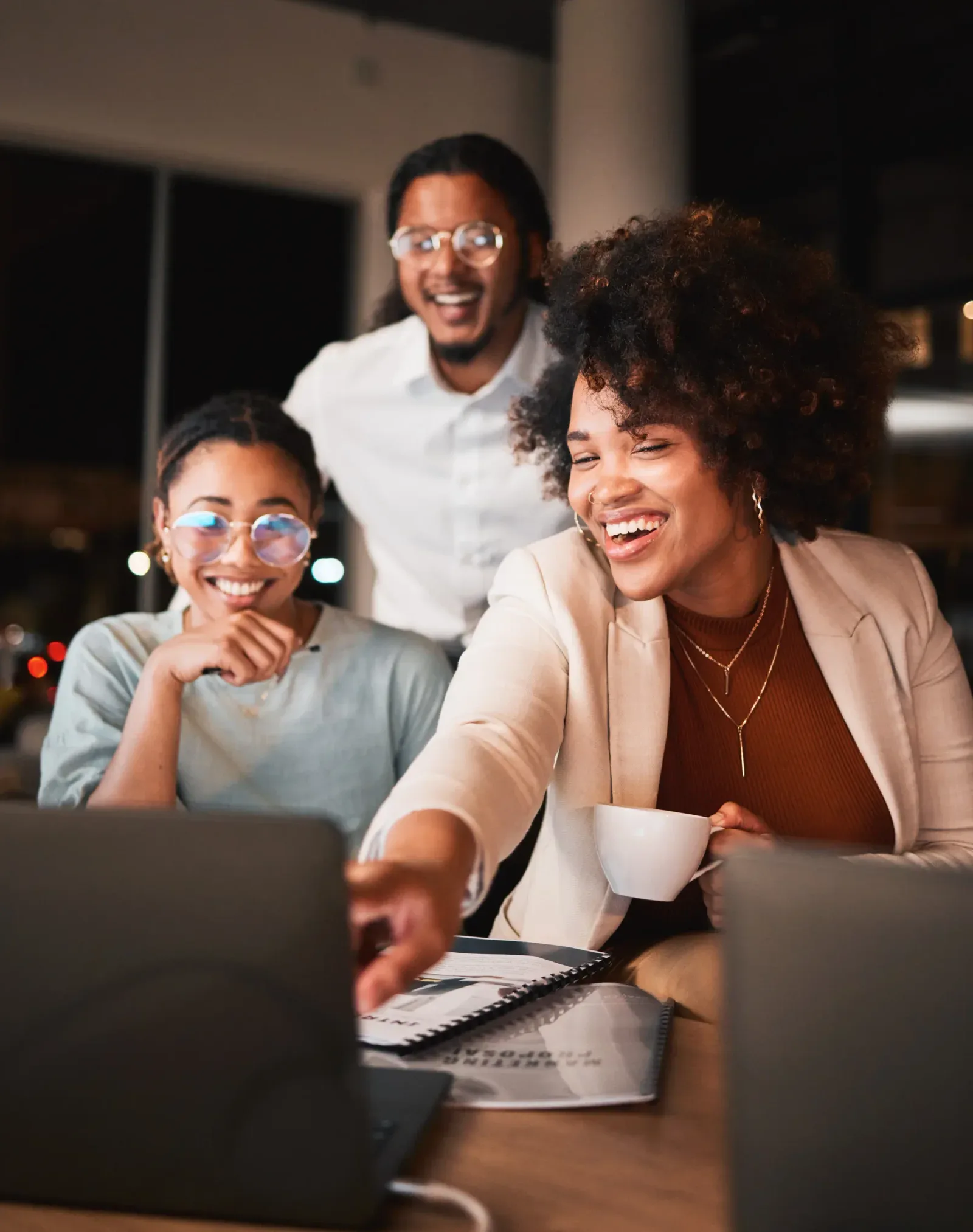 Three colleagues smiling at a laptop as they review their team’s training progress